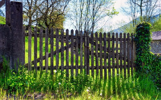 A wooden gate with a gate on the right side. The gate is surrounded by grass and flowers