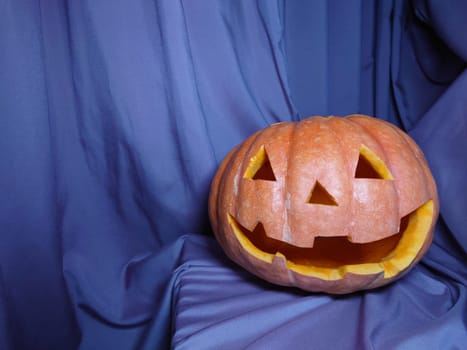 Funny orange pumpkin for Halloween on a lilac fabric background with a space for text close-up