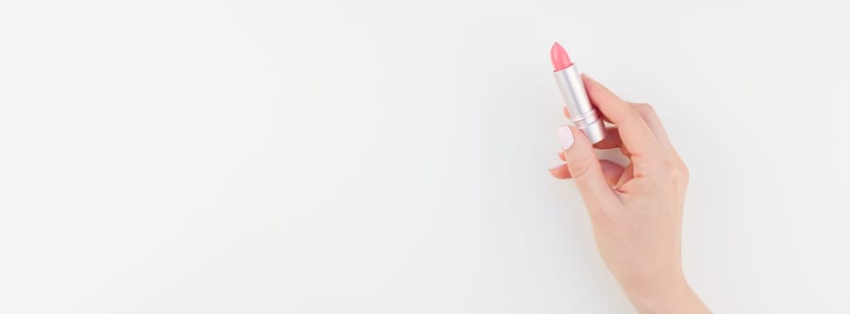 Woman hand with pastel manicure polish holding pink lipstick isolated on white background with copy space. Long wide banner for feminine beauty blog social media