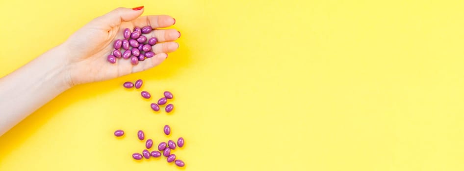Woman hand holding purple pills handful isolated on bold yellow background with copy space. Template for feminine beauty blog social media. Female healthcare or suicide prevention concept