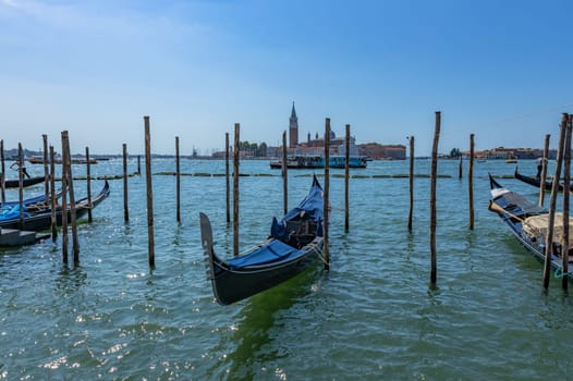 Venice, Italy - July 26, 2024: Gondolas against the San Giorgio island in Venice, Italy. Gondola is the most attractive tourist transport in Venice. Traveling and vacation in sunny Venice.