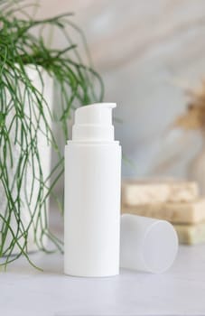 White cream pump bottle on white marble countertop near potted green plant in bathroom, close up, packaging mockup. Natural cosmetic product for face or body care