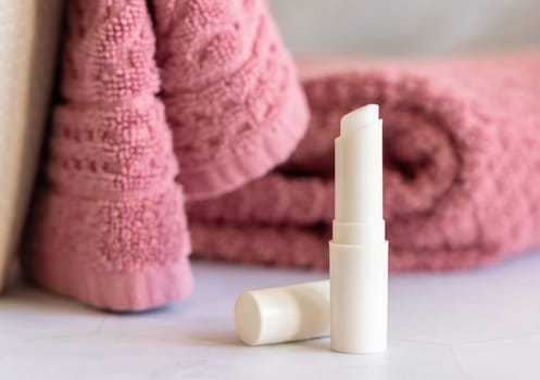 Opened lip balm stick on marble countertop near pink folded towel in bathroom, closeup, cosmetic mockup. Lifestile scene with beauty product, everyday lip care routine
