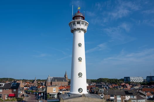 The approx. 28 m high white lighthouse J.C.J. van Speijk in Egmond aan Zee, North Holland, Netherlands with some of the town's houses