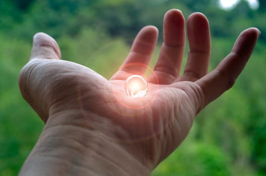 Shining marble on top of human hand with blurred nature background.