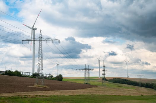 Electric power pole and windmills in a field, transformation to renewable sustainable energy, electricity generator, environmental conversation