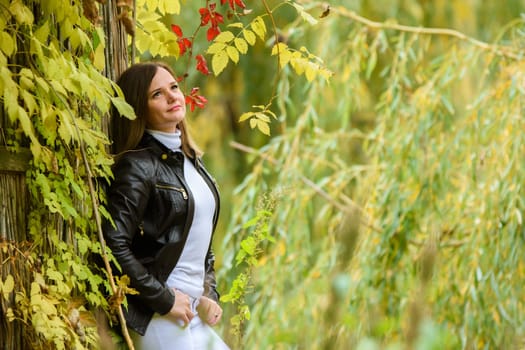 A young beautiful girl pressed her back against a wooden wall and looks at the autumn forest