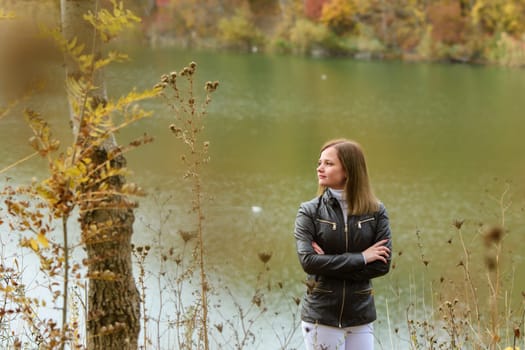 A girl stands by the lake on a warm autumn day and looks thoughtfully into the distance.