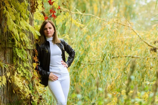 A young beautiful girl leans on a wooden wall against the backdrop of an autumn forest and looks into the frame