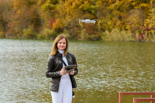 A young beautiful girl launches a radio-controlled quadcopter on the shore of an autumn lake, the girl looks into the frame