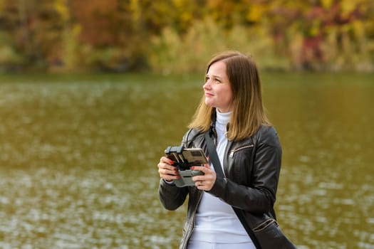 A young beautiful girl launches a radio-controlled quadcopter on the shore of an autumn lake, the girl looks at the drone