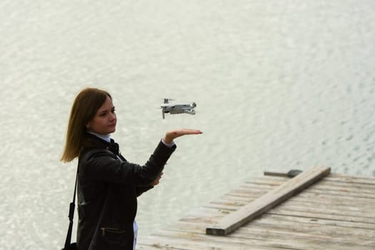 A young beautiful girl launches a radio-controlled quadcopter on the shore of a lake, the drone lands on the girl's hand