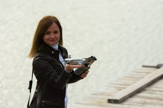 A young beautiful girl launches a radio-controlled quadcopter on the shore of a lake, the drone landed on the girl's hand