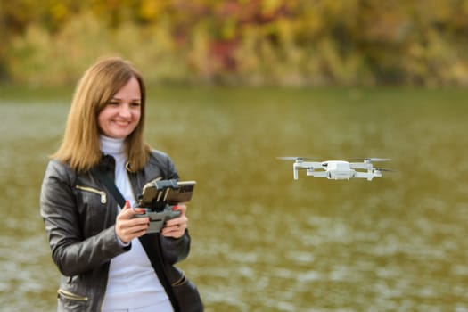 A young beautiful girl launches a radio-controlled quadcopter on the shore of an autumn lake, the girl looks at the drone smiling