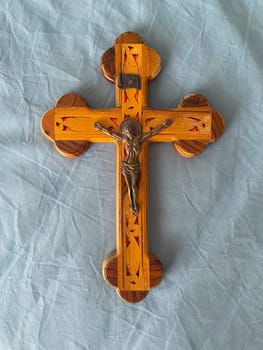 Crafted wooden crucifix with a detailed metal figure of Jesus Christ lies on a blue fabric background. Spiritual and religion concept.