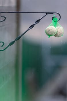 2 bird fat balls in a green net hanging outside to feed birds in the winter with snow coming down