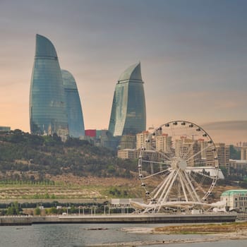 The skyline of Baku, Azerbaijan features distinct flame towers alongside Baku Eye Ferris wheel, showcasing a blend of modern architecture bathed in warm evening light