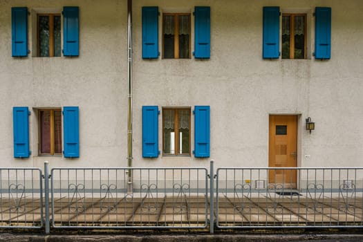 Exterior of a building with five windows with open blue shutters and a brown front door