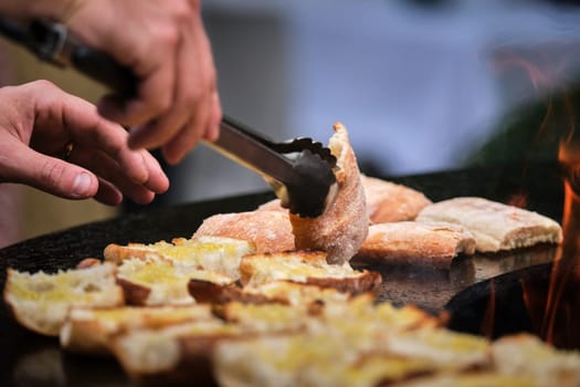 close-up detail view of chef flipping sandwiches grilled at round steel iron firepit hearth table surface brazier, red fire, barbecue