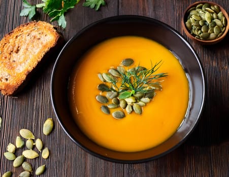 Homemade pumpkin soup with seeds and dill on rustic wooden table.