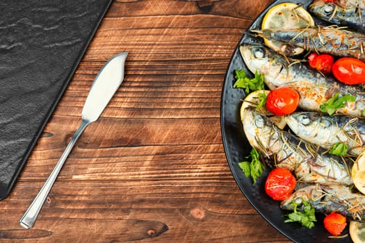 Baked sardine fish with lemon, cherry tomatoes and rosemary on ceramic plate on rustic wooden table. Healthy and tasty dinner. Copy space.