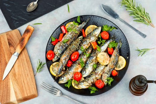 Baked sardine fish with lemon, cherry tomatoes and rosemary on ceramic plate on rustic wooden table. Healthy and tasty dinner. Copy space.