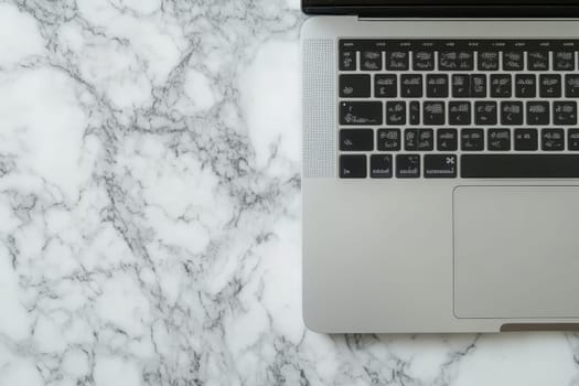 Modern laptop partially visible on white marble surface, showcasing sleek design and luxurious workspace aesthetic.