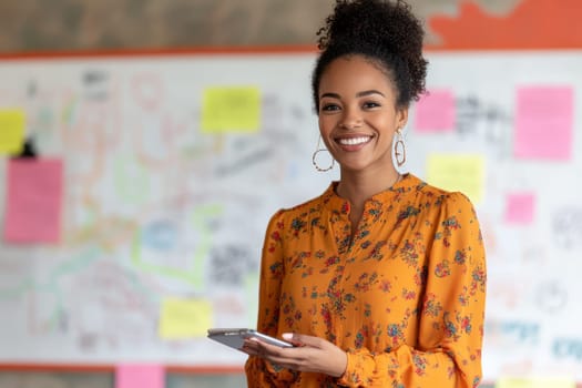 Cheerful woman in orange floral blouse holding digital tablet in office with colorful sticky notes in background.