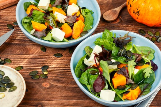 Green salad with Hokkaido pumpkin and cheese and greens. Healthy homemade food on wooden rustic background.