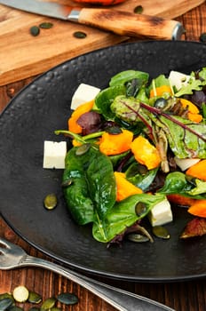 Green salad with Hokkaido pumpkin and cheese and greens. Healthy homemade food on wooden rustic background.