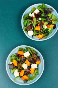 Green salad with Hokkaido pumpkin and cheese and greens. Healthy homemade food on wooden rustic background.