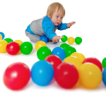 Comical child playing with colored plastic balls on white floor