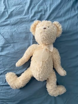 Soft and cuddly teddy bear lies on a light blue fabric surface, exuding warmth and comfort. Timeless design evokes feelings of childhood nostalgia and tranquility.