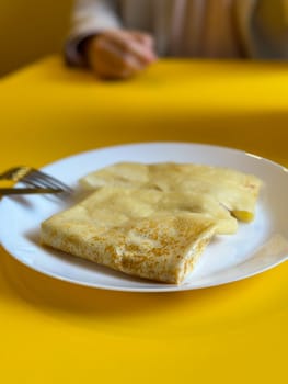 Breakfast setting with a plate of crepes and a frothy cappuccino on a bright yellow table. Cafe with modern design. Pancakes with different fillings.