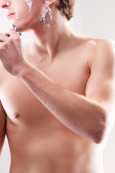 Young man carefully shaving his face with a razor in the bathroom, creating foam for a smooth shave and feeling fresh and confident