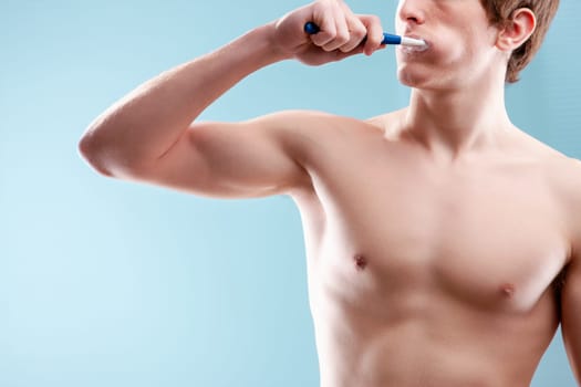 Young man brushing his teeth in the bathroom, focusing on oral hygiene and personal care with a fit body and a calming blue backdrop
