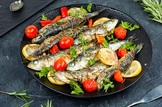 Sardines roasted with cherry tomatoes rosemary and lemon on table.