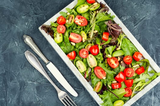 Juicy salad with cherry tomatoes and fresh lettuce leaves on a modern stone tray. Space for text.