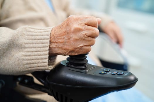 Asian elderly disability woman patient use joystick electric wheelchair in hospital.