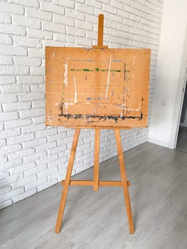 An artist's easel stands elegantly against a textured white brick wall, with well-used wooden canvas holder. Creativity and artistic expression concept.