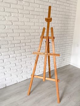 An artist's easel stands elegantly against a textured white brick wall, with well-used wooden canvas holder. Creativity and artistic expression concept.