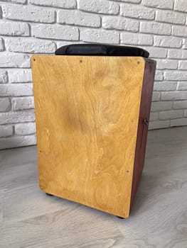 Cajon drum sits elegantly against a textured white brick wall, highlighting its wooden craftsmanship. Musical Instrument for creating music at home and hobby concept.
