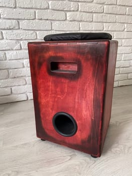 Cajon drum sits elegantly against a textured white brick wall, highlighting its wooden craftsmanship. Musical Instrument for creating music at home and hobby concept.