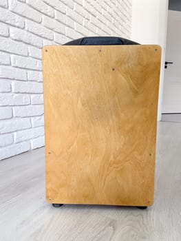 Cajon drum sits elegantly against a textured white brick wall, highlighting its wooden craftsmanship. Musical Instrument for creating music at home and hobby concept.
