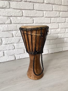 Traditional djembe drum stands in front of a textured white brick wall. Musical instrument and ethnic music concept.