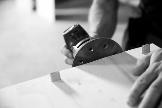 Skilled carpenter sanding wood with electric sander in workshop, creating smooth finish. Sawdust fills air as craftsman focuses on precision, showcasing woodworking artistry. - black n white -