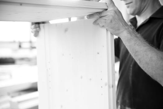 Carpenter is assembling a piece of wooden furniture in his workshop, his experienced hands carefully aligning the pieces. - black n white -