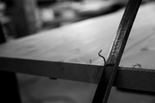 Close up of a wooden plank being worked with traditional tools by a carpenter in a workshop. - black n white -