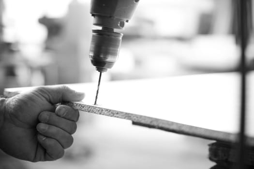 Carpenter is using a drill press to make a hole in a wood plank in his workshop. - black n white -