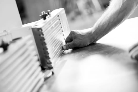 Carpenter in a busy workshop carefully uses a planer machine to smooth wood, showing craftsmanship and dedication in black and white. - black n white -
